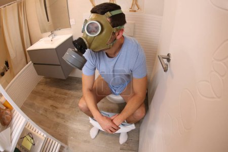 Téléchargez les photos : Wide angle shot of young man with gas mask in toilet - en image libre de droit