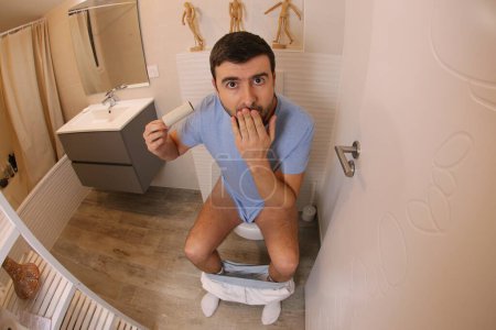 Téléchargez les photos : Wide angle shot of young man with empty paper roll in toilet - en image libre de droit