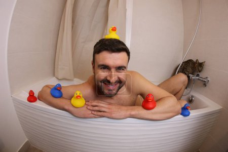Foto de Wide angle shot of handsome young man with rubber ducks in bath - Imagen libre de derechos