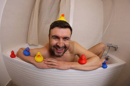 Photo for Wide angle shot of handsome young man with rubber ducks in bath - Royalty Free Image