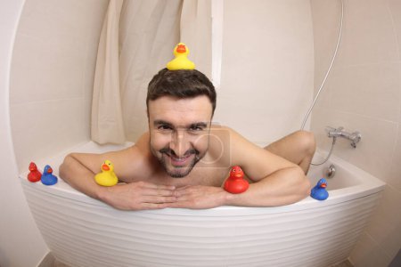 Foto de Wide angle shot of handsome young man with rubber ducks in bath - Imagen libre de derechos