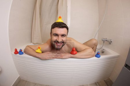 Téléchargez les photos : Plan grand angle de beau jeune homme avec des canards en caoutchouc dans le bain - en image libre de droit