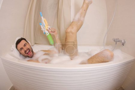 Photo for Wide angle shot of handsome young man playing with water gun in bath - Royalty Free Image