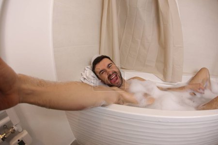 Foto de Amplio ángulo de tiro de joven guapo hablando selfie en baño - Imagen libre de derechos