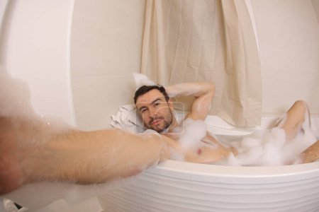 Téléchargez les photos : Plan grand angle de beau jeune homme parlant selfie dans le bain - en image libre de droit