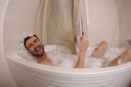 Téléchargez les photos : Wide angle shot of handsome young man reading book in bath - en image libre de droit
