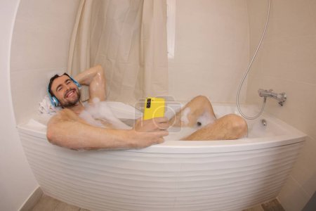 Téléchargez les photos : Plan grand angle de beau jeune homme avec écouteurs écouter de la musique dans le bain - en image libre de droit