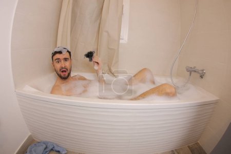 Photo for Wide angle shot of shocked young man holding hair in his hand in bath - Royalty Free Image