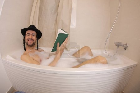 Téléchargez les photos : Plan grand angle de beau jeune homme en chapeau juif lisant tora dans le bain - en image libre de droit