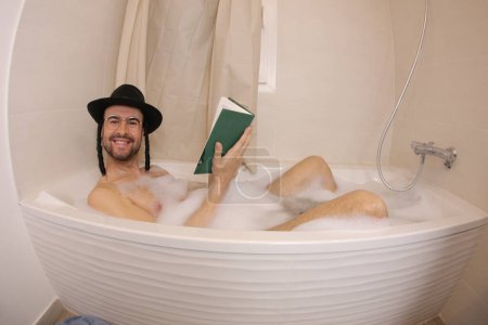 Foto de Amplio ángulo de tiro de joven guapo en sombrero judío leyendo tora en baño - Imagen libre de derechos