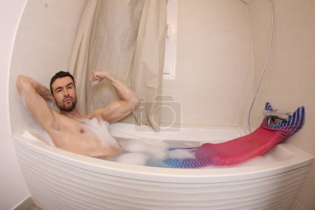 Téléchargez les photos : Wide angle shot of handsome young man in mermaid costume in bath - en image libre de droit