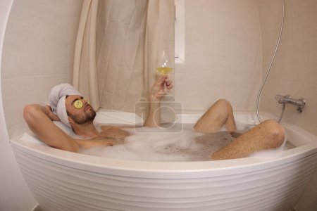Téléchargez les photos : Wide angle shot of handsome young man with glass of champagne in bath - en image libre de droit