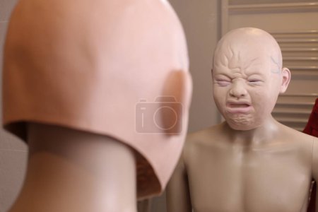 Foto de Primer plano de maniquí con la máscara de bebé llorando delante del espejo en casa - Imagen libre de derechos