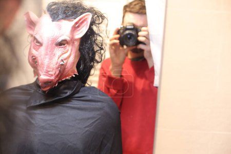 Téléchargez les photos : Gros plan de la personne dans effrayante masque de porc devant le miroir à la maison - en image libre de droit