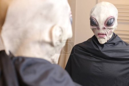 Téléchargez les photos : Gros plan de la personne en masque extraterrestre devant le miroir à la maison - en image libre de droit