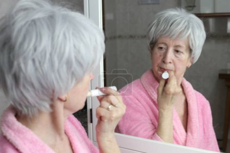 Photo for Close-up portrait of mature woman applying lip balm in front of mirror in bathroom - Royalty Free Image