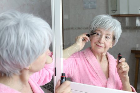 Téléchargez les photos : Portrait en gros plan de femme mature faisant du maquillage devant le miroir dans la salle de bain - en image libre de droit