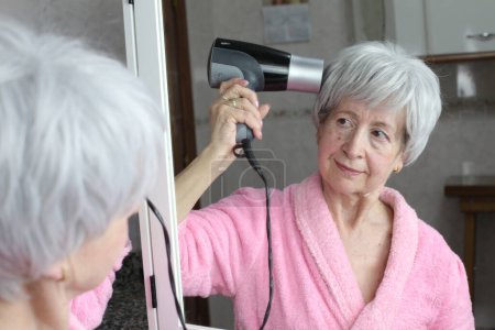 Foto de Primer plano retrato de mujer madura con secador de pelo delante del espejo en el baño - Imagen libre de derechos