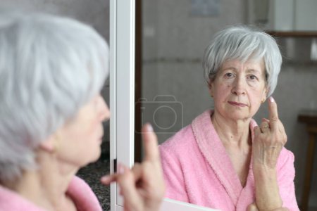 Photo for Close-up portrait of mature woman showing middle finger in front of mirror in bathroom - Royalty Free Image