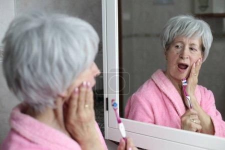 Foto de Primer plano retrato de la mujer madura cepillarse los dientes delante del espejo en el baño - Imagen libre de derechos