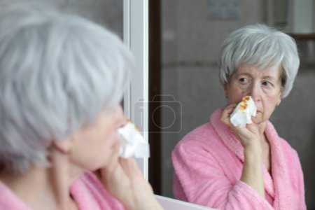Photo for Close-up portrait of mature woman with bleeding nose in front of mirror in bathroom - Royalty Free Image