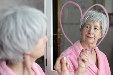 Photo for Close-up portrait of mature woman in front of mirror in bathroom with heart shape drawing - Royalty Free Image