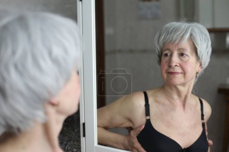 Téléchargez les photos : Portrait en gros plan de femme mature avec soutien-gorge noir devant le miroir dans la salle de bain - en image libre de droit
