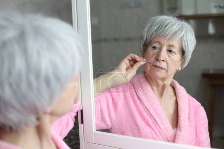 Foto de Primer plano retrato de la mujer madura tirando de pelo facial delante del espejo en el baño - Imagen libre de derechos
