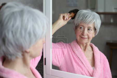 Foto de Retrato de cerca de la mujer madura cepillarse el pelo delante del espejo en el baño - Imagen libre de derechos
