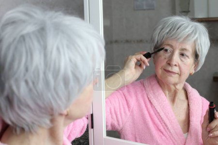 Photo for Close-up portrait of mature woman doing makeup in front of mirror in bathroom - Royalty Free Image