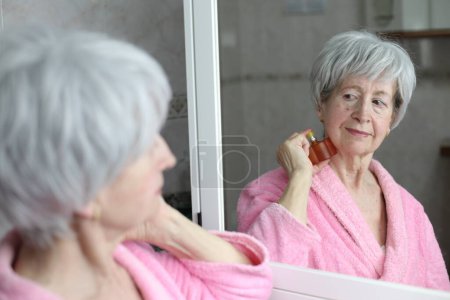Foto de Primer plano retrato de la mujer madura aplicando perfume delante del espejo en el baño - Imagen libre de derechos