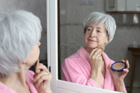 Photo for Close-up portrait of mature woman doing makeup in front of mirror in bathroom - Royalty Free Image