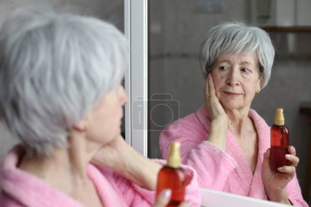Foto de Primer plano retrato de la mujer madura haciendo rutina de cuidado de la piel delante del espejo en el baño - Imagen libre de derechos