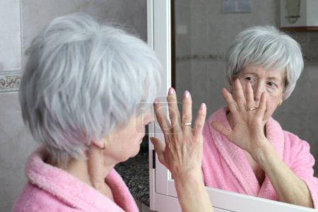 Téléchargez les photos : Portrait en gros plan de femme mature devant le miroir dans la salle de bain - en image libre de droit