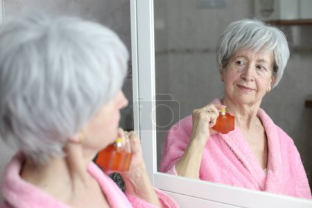 Photo for Close-up portrait of mature woman applying perfume in front of mirror in bathroom - Royalty Free Image