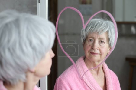 Téléchargez les photos : Portrait en gros plan de la femme mûre devant le miroir dans la salle de bain dessin forme de coeur - en image libre de droit