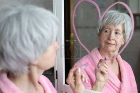 Photo for Close-up portrait of mature woman in front of mirror in bathroom drawing heart shape - Royalty Free Image