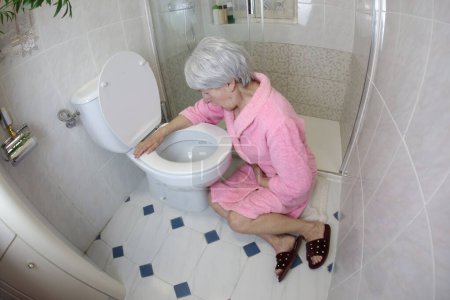 Photo for Wide angle shot of senior woman sitting near toilet at bathroom, food poisoning - Royalty Free Image
