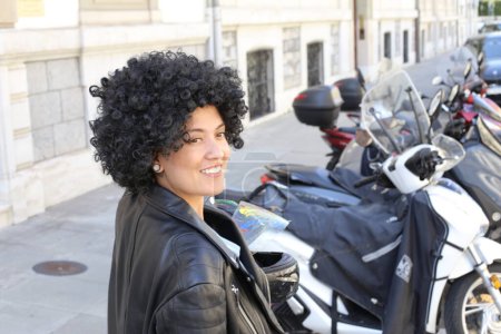 Foto de Retrato de una hermosa joven en chaqueta de cuero con pelo rizado delante de bicicletas estacionadas en la calle de la ciudad - Imagen libre de derechos