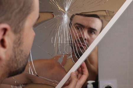 Téléchargez les photos : Portrait de jeune homme devant miroir brisé dans la salle de bain - en image libre de droit
