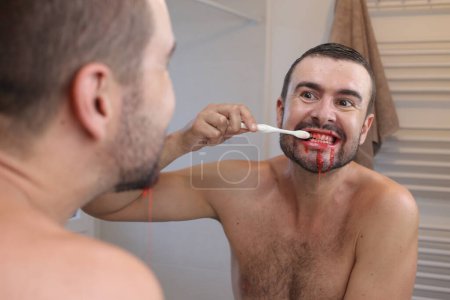 Foto de Retrato de un joven con encías sangrantes cepillándose los dientes delante del espejo en el baño - Imagen libre de derechos