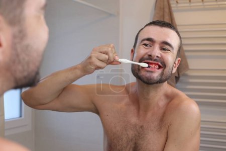 Foto de Retrato de un joven con encías sangrantes cepillándose los dientes delante del espejo en el baño - Imagen libre de derechos