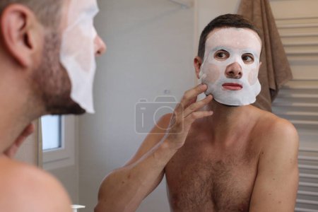 Photo for Portrait of young man with skin mask in front of mirror in bathroom - Royalty Free Image