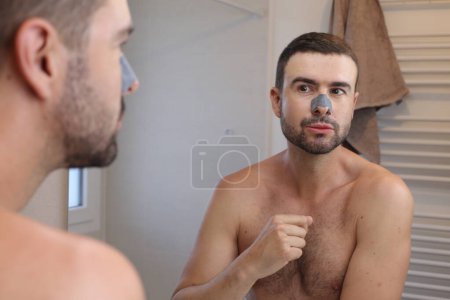 Foto de Retrato de hombre joven con máscara de piel en la nariz delante del espejo en el baño - Imagen libre de derechos