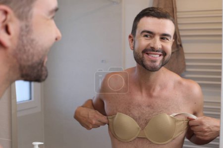 Téléchargez les photos : Portrait de jeune homme avec soutien-gorge devant miroir dans la salle de bain - en image libre de droit