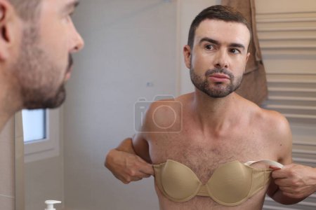Photo for Portrait of young man with bra in front of mirror in bathroom - Royalty Free Image