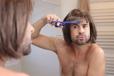Téléchargez les photos : Portrait de jeune homme faisant coupe de cheveux devant le miroir dans la salle de bain - en image libre de droit