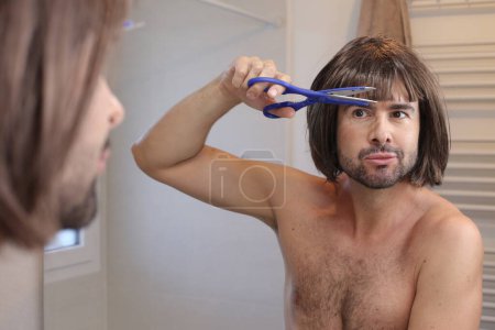 Téléchargez les photos : Portrait de jeune homme faisant coupe de cheveux devant le miroir dans la salle de bain - en image libre de droit