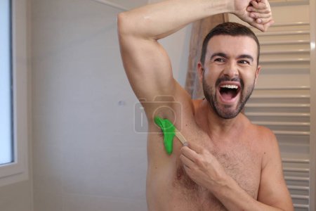 Téléchargez les photos : Portrait de jeune homme épilant ses aisselles devant le miroir dans la salle de bain - en image libre de droit