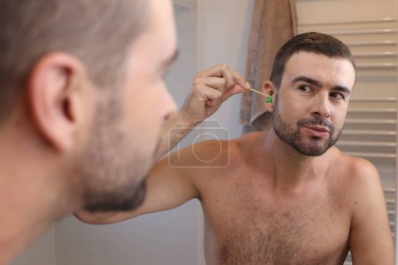 Photo for Portrait of young man waxing his ear hair in front of mirror in bathroom - Royalty Free Image